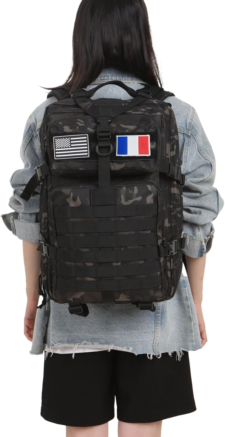 Back view of a person wearing a black camouflage tactical backpack with US and French flag patches over a denim jacket.