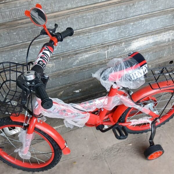 Red kids' bicycle with training wheels and baskets front and rear, wrapped in plastic, leaning against a metal shutter.