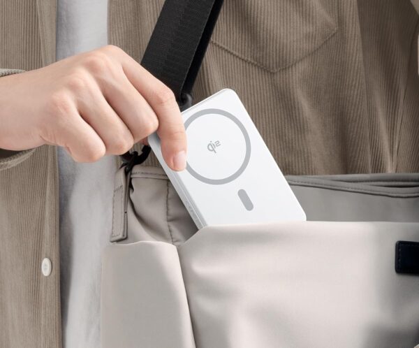 Person places a white wireless charging card into a beige bag using a black strap.
