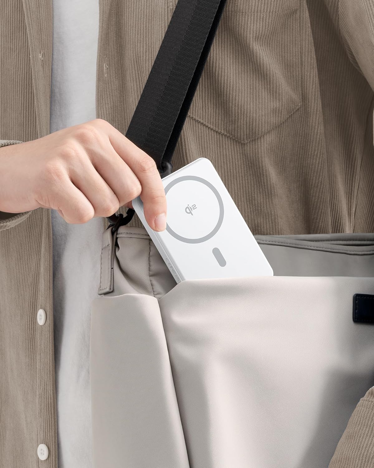 Person places a white wireless charging card into a beige bag using a black strap.