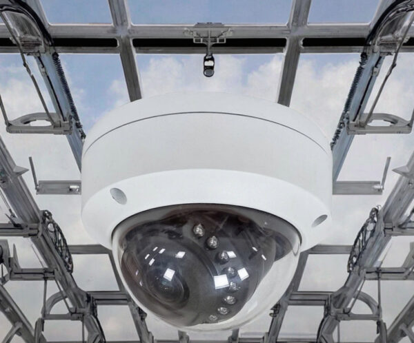 Dome surveillance camera mounted on a metal frame against a blue sky backdrop, surveillance setup visible above.