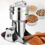 Stainless steel electric spice grinder with cinnamon sticks and bowls of spices in the background.