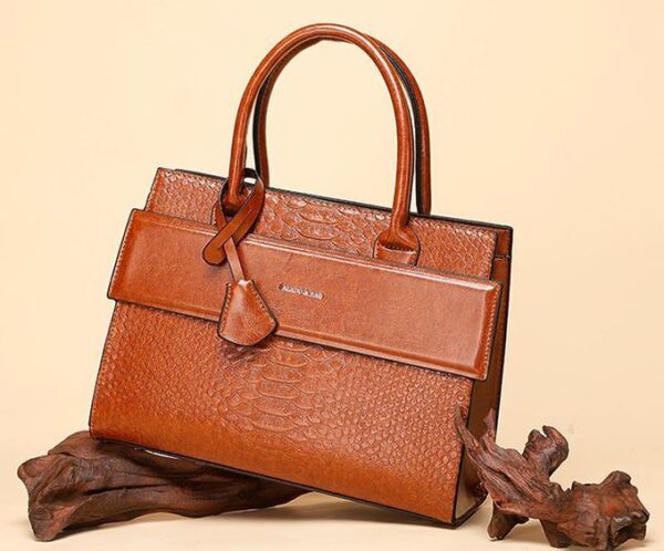 Brown crocodile-embossed leather handbag with top handles and front flap on a beige background.