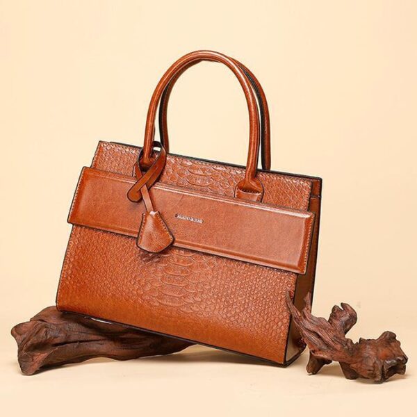 Brown crocodile-embossed leather handbag with top handles and front flap on a beige background.