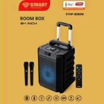 Portable Bluetooth boom box with a blue-lit front speaker, carrying handle, two wireless mics, and a tall remote on a yellow background (SHTP-8088M).