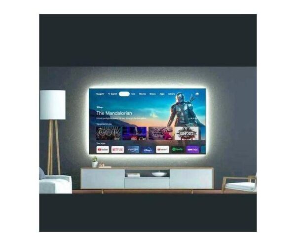 Living room with a large flat-screen TV on a console, glowing on a dark wall and surrounded by a lamp and seating area.