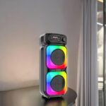 Bluetooth speaker with two stacked rainbow LED panels on a table by a window.