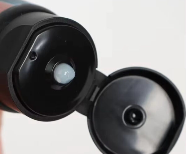 Close-up of a black flip-top bottle cap opened, exposing the inner seal and small nozzle.