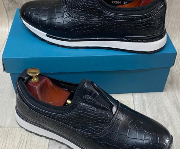 Black crocodile-embossed slip-on sneakers with white cushioned sole, displayed on a blue shoe box.