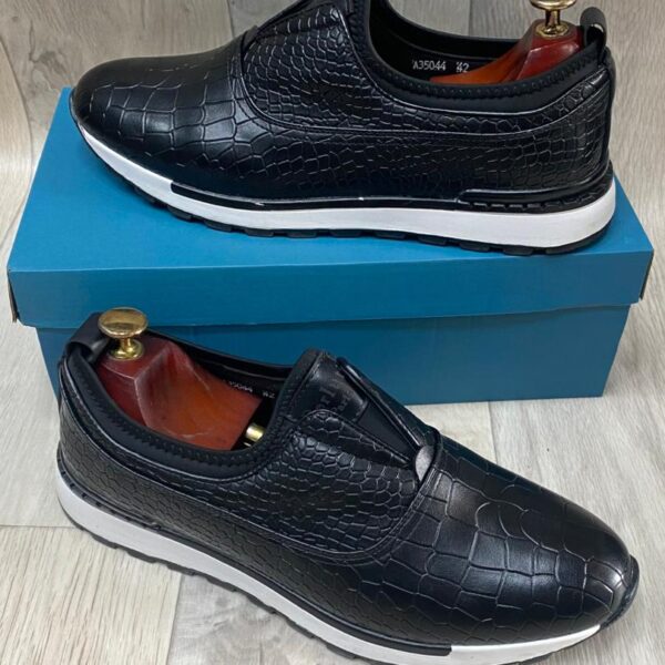 Black crocodile-embossed slip-on sneakers with white cushioned sole, displayed on a blue shoe box.