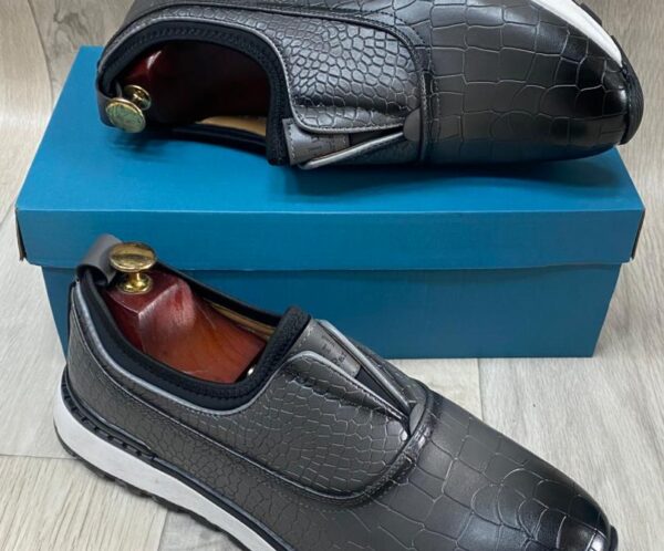 Grey crocodile-textured slip-on sneakers with white soles resting on a blue box.