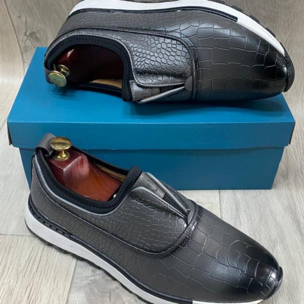 Grey crocodile-textured slip-on sneakers with white soles resting on a blue box.