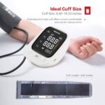 Digital blood pressure monitor with a black display and a cuff laid out beside it on a white surface.