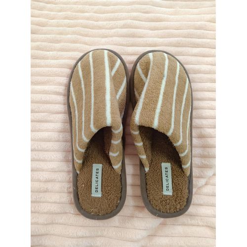 Pair of beige striped slippers placed side by side on a pale pink rug, with 'DELICATES' labels inside.