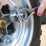 Close-up of a person using a chrome socket wrench to tighten lug nuts on a motorcycle wheel rim.