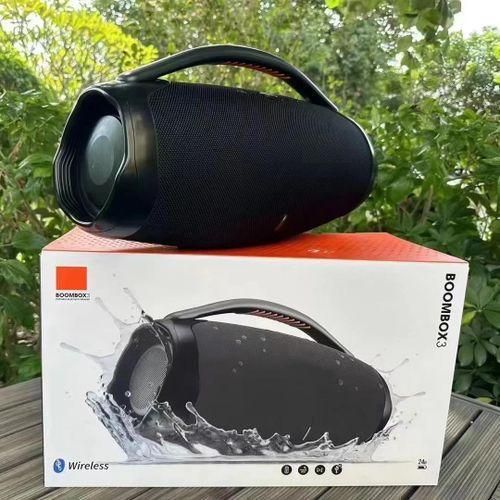 Black Bluetooth speaker with a handle rests on top of its box outdoors, with greenery in the background and a splash image on the packaging.