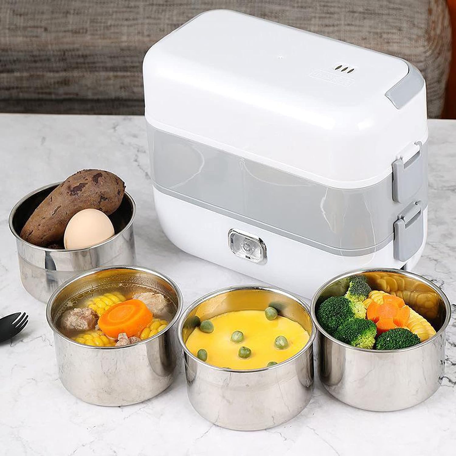 White electric lunch box on a marble counter surrounded by five stainless steel food containers with mixed meals like corn, broccoli, and vegetables.
