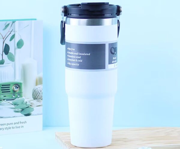 White insulated travel mug with a black lid on a wooden board against a light blue background, product shot.