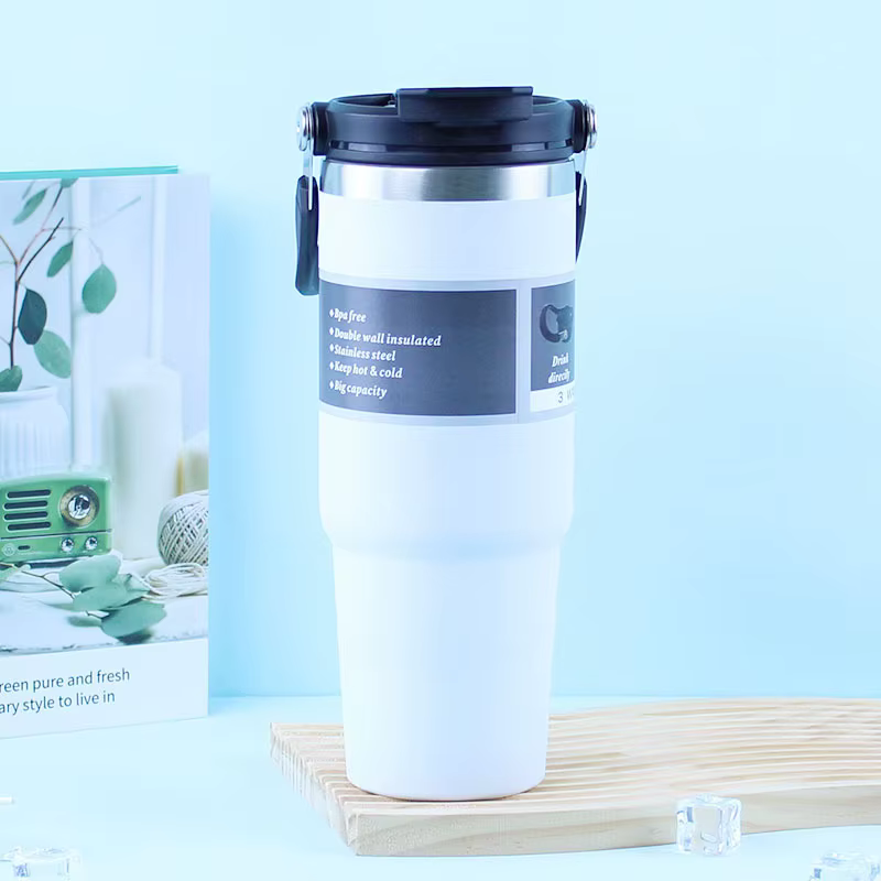 White insulated travel mug with a black lid on a wooden board against a light blue background, product shot.