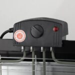 Close-up of a black grill control unit with a rotary dial, red indicator light, and a 'Do Not Touch' sticker.